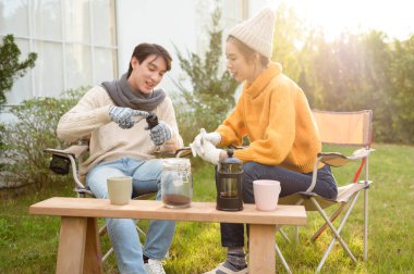 İki arkadaş bahçede dinlenir, sıcak içkilerini yudumlar ve güneşli bir günde sohbet ederler..