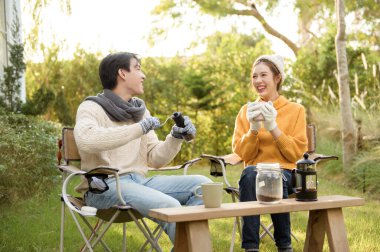 İki arkadaş bahçede dinlenir, sıcak içkilerini yudumlar ve güneşli bir günde sohbet ederler..
