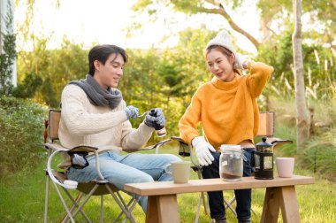 İki arkadaş bahçede dinlenir, sıcak içkilerini yudumlar ve güneşli bir günde sohbet ederler..