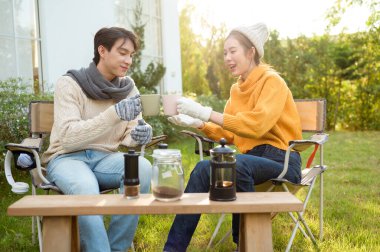 İki arkadaş bahçede dinlenir, sıcak içkilerini yudumlar ve güneşli bir günde sohbet ederler..