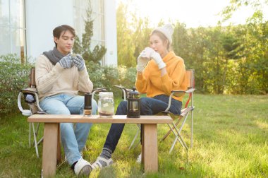 İki arkadaş bahçede dinlenir, sıcak içkilerini yudumlar ve güneşli bir günde sohbet ederler..
