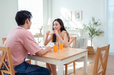 Genç bir çift, sıcak güneş ışığı ve dekorasyonlarla çevrili, neşeli bir kahvaltı yapar..