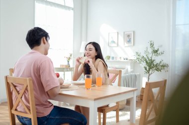 Genç bir çift, sıcak güneş ışığı ve dekorasyonlarla çevrili, neşeli bir kahvaltı yapar..