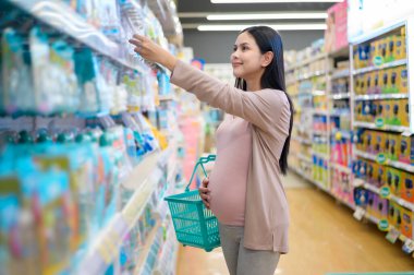 Güzel hamile bir kadın alışveriş merkezinde yeni doğan ürünleri alıp bebek için hazırlanıyor..