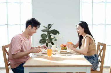 Genç bir çift, sıcak güneş ışığı ve dekorasyonlarla çevrili, neşeli bir kahvaltı yapar..