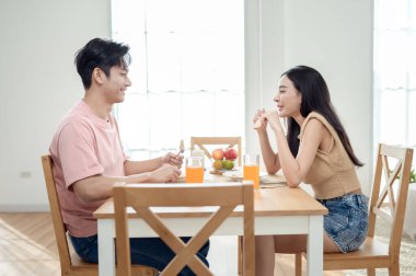 Genç bir çift, sıcak güneş ışığı ve dekorasyonlarla çevrili, neşeli bir kahvaltı yapar..