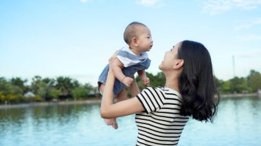 Bir anne, bebeğiyle güneşli göl kenarında neşeli bir anın tadını çıkarır..
