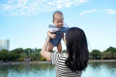 Bir anne, bebeğiyle güneşli göl kenarında neşeli bir anın tadını çıkarır..