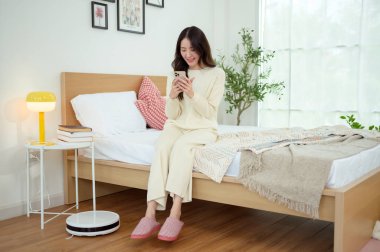 Robotik elektrikli süpürge çalışırken Asyalı genç kadın dinleniyor.