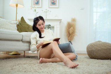 Genç Asyalı kadın oturma odasında kitap okumaktan zevk alıyor.