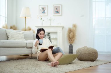 Genç Asyalı kadın oturma odasında kitap okumaktan zevk alıyor.