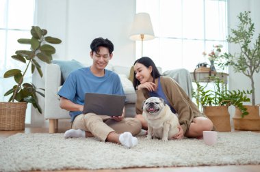 Genç bir çift, köpekleriyle bir kanepede rahatlar. Parlak bir yaşam alanında keyifli anlar paylaşırlar..