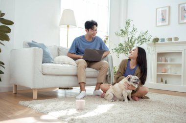 Genç bir çift, köpekleriyle bir kanepede rahatlar. Parlak bir yaşam alanında keyifli anlar paylaşırlar..