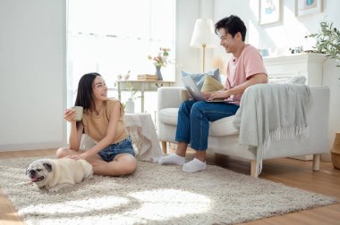 Genç bir çift, köpekleriyle bir kanepede rahatlar. Parlak bir yaşam alanında keyifli anlar paylaşırlar..