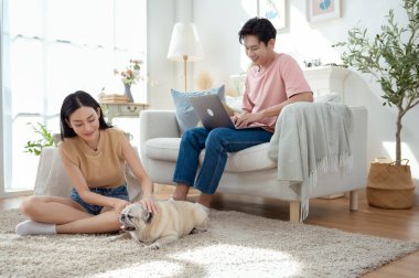 Genç bir çift, köpekleriyle bir kanepede rahatlar. Parlak bir yaşam alanında keyifli anlar paylaşırlar..