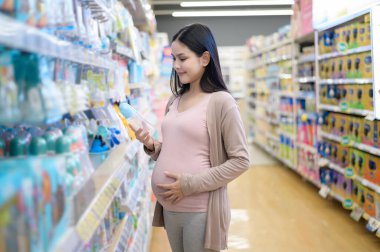 Güzel hamile bir kadın alışveriş merkezinde yeni doğan ürünleri alıp bebek için hazırlanıyor..