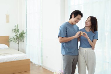 Parlak bir yaşam alanında küçük bir ev modelini tutarken çift neşeyle gülümsüyor..