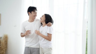 Bir çift yakın duruyor, gülümsüyor ve güneş ışığında bir bardak su tutuyor..