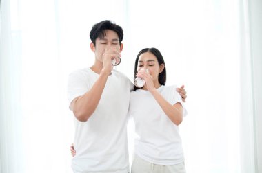 Bir çift yakın duruyor, gülümsüyor ve güneş ışığında bir bardak su tutuyor..