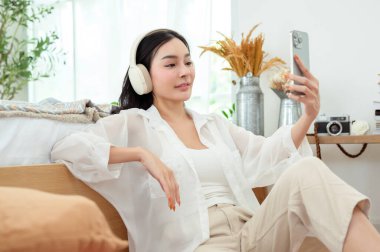 Genç Asyalı kadın yatakta uzanmış akıllı telefon kullanıyor.