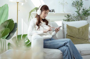 Kulaklıkla müzik dinleyen, rahat bir koltukta otururken gülümseyen biri..