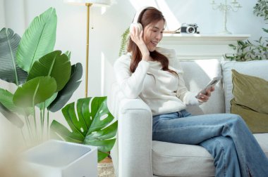 Kulaklıkla müzik dinleyen, rahat bir koltukta otururken gülümseyen biri..