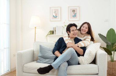 Genç bir çift kanepede dinleniyor. Parlak bir oturma odasında bitkilerle keyifli bir anı paylaşıyorlar..