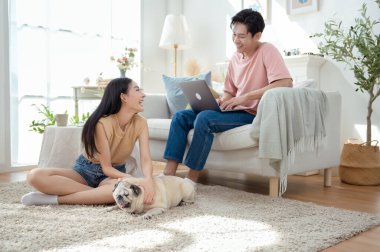 Genç bir çift, köpekleriyle bir kanepede rahatlar. Parlak bir yaşam alanında keyifli anlar paylaşırlar..