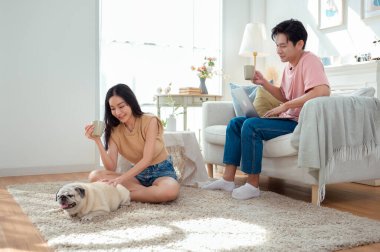 Genç bir çift, köpekleriyle bir kanepede rahatlar. Parlak bir yaşam alanında keyifli anlar paylaşırlar..