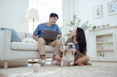 Genç bir çift, köpekleriyle bir kanepede rahatlar. Parlak bir yaşam alanında keyifli anlar paylaşırlar..