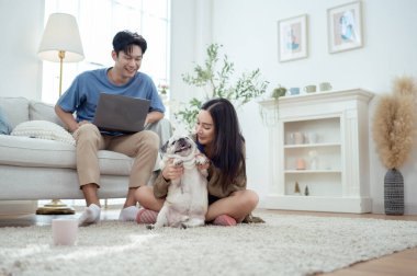 Genç bir çift, köpekleriyle bir kanepede rahatlar. Parlak bir yaşam alanında keyifli anlar paylaşırlar..