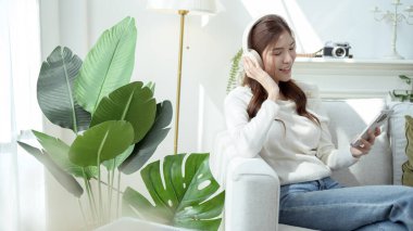 Kulaklıkla müzik dinleyen, rahat bir koltukta otururken gülümseyen biri..