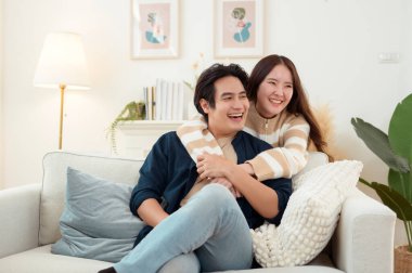 Genç bir çift kanepede dinleniyor. Parlak bir oturma odasında bitkilerle keyifli bir anı paylaşıyorlar..