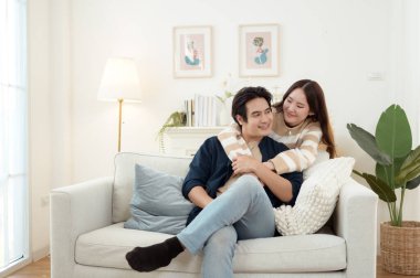 Genç bir çift kanepede dinleniyor. Parlak bir oturma odasında bitkilerle keyifli bir anı paylaşıyorlar..