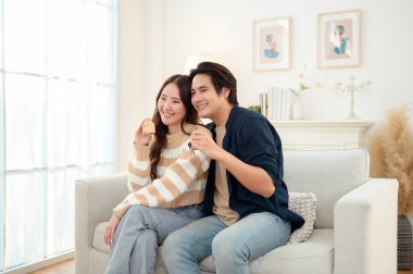 Genç bir çift kanepede dinleniyor. Parlak bir oturma odasında bitkilerle keyifli bir anı paylaşıyorlar..