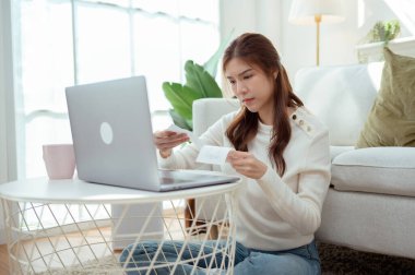 Bir kadın dizüstü bilgisayarı üzerinde çalışırken yerde oturuyor, gülümsüyor ve faturaları düzenliyor..