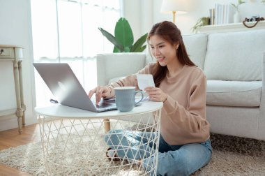 Bir kadın dizüstü bilgisayarı üzerinde çalışırken yerde oturuyor, gülümsüyor ve faturaları düzenliyor..