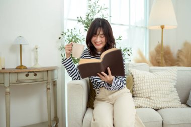 Genç bir kadın kanepede oturuyor, rahat bir ev ortamında bir kitaba dalmış..