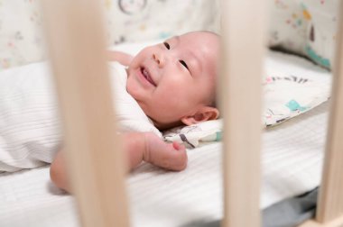 Neşeli bir bebek beşiğinde yatar, gülümserken merakla çevrelerini keşfeder..