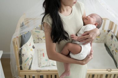 Bir kadın bebeğini sevgiyle kucağına alır. Yumuşak ışıkla dolu bir bebek odasında..