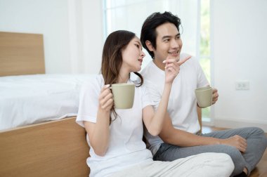 Sabah ışığıyla dolu bir yatak odasında iki kişi kahkaha atıp kahve yudumluyor..