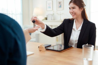 Bir emlakçı modern bir ofiste gülümseyen bir çifte ev anahtarlarını verir..