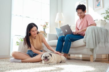 Genç bir çift, köpekleriyle bir kanepede rahatlar. Parlak bir yaşam alanında keyifli anlar paylaşırlar..