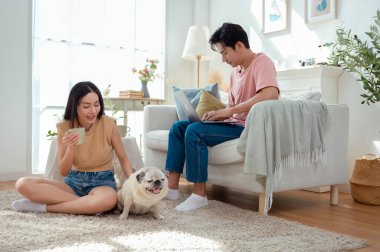 Genç bir çift, köpekleriyle bir kanepede rahatlar. Parlak bir yaşam alanında keyifli anlar paylaşırlar..