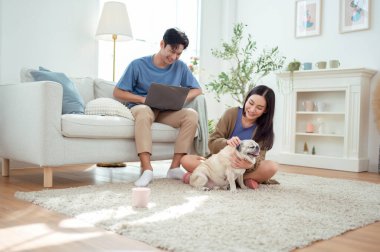 Genç bir çift, köpekleriyle bir kanepede rahatlar. Parlak bir yaşam alanında keyifli anlar paylaşırlar..