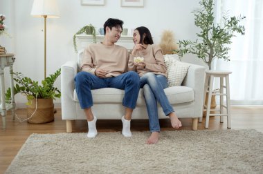 İki kişi, şık bir oturma odasında rahat bir kanepede otururken aynı kahkahayı paylaşıyor..