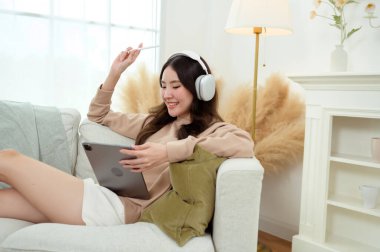 Evdeki oturma odasında tablet kullanan genç Asyalı kadın.