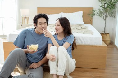 Genç bir çift, sıcak yatak odalarının zemininde dinlenirken patlamış mısır paylaşır ve gülümser..