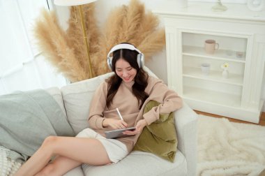 Evdeki oturma odasında tablet kullanan genç Asyalı kadın.