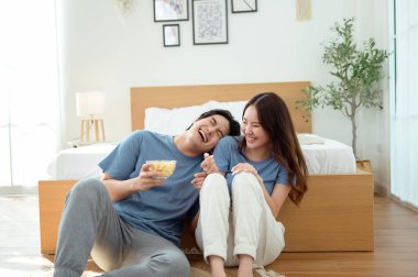 Genç bir çift, sıcak yatak odalarının zemininde dinlenirken patlamış mısır paylaşır ve gülümser..